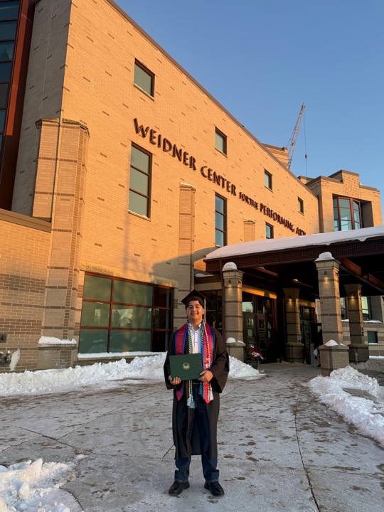 Bibesh Pyakurel in graduation regalia outside the Weidner Center at UW–Green Bay